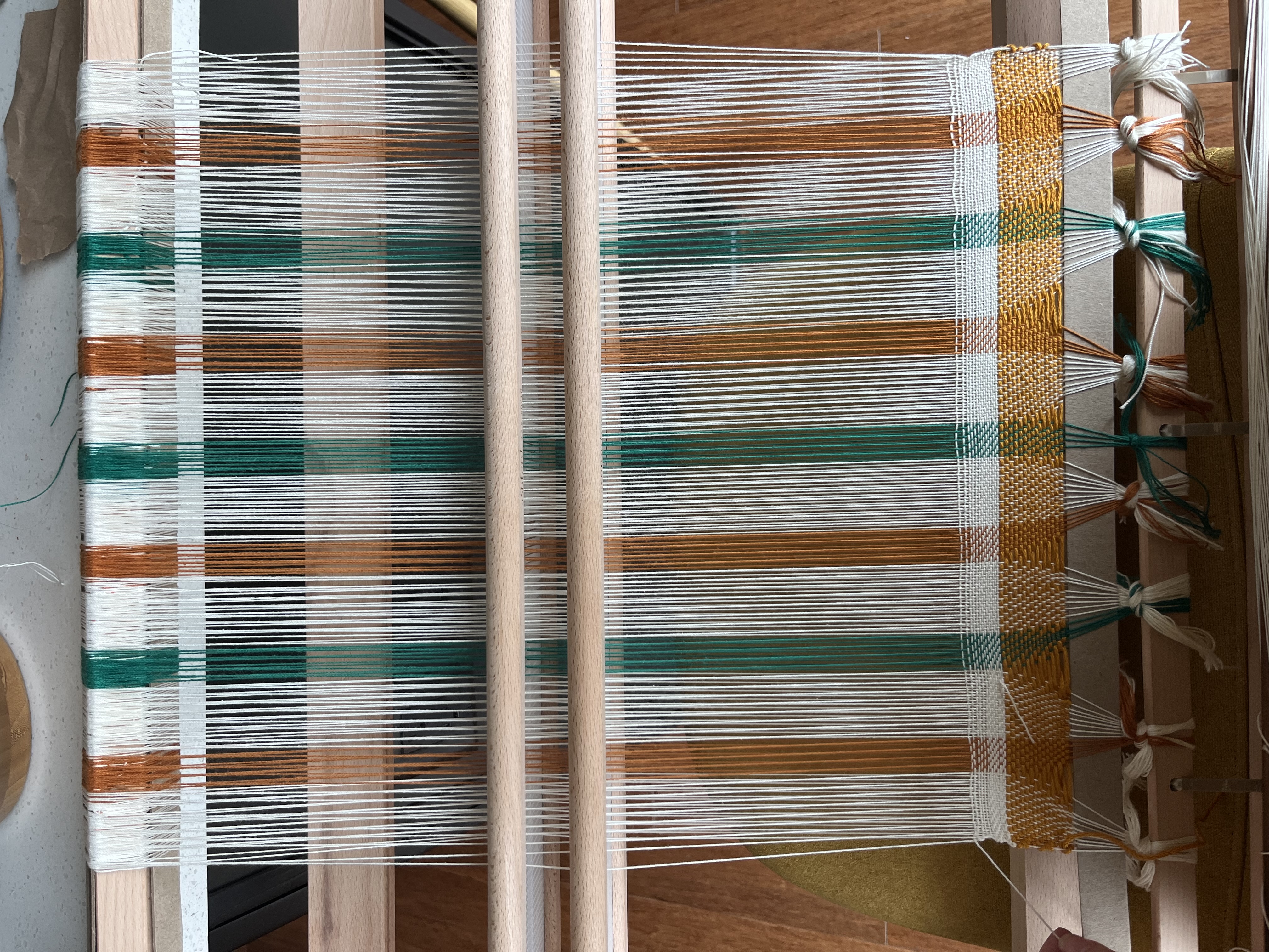 Photo of a warped loom with white, green, and orange.